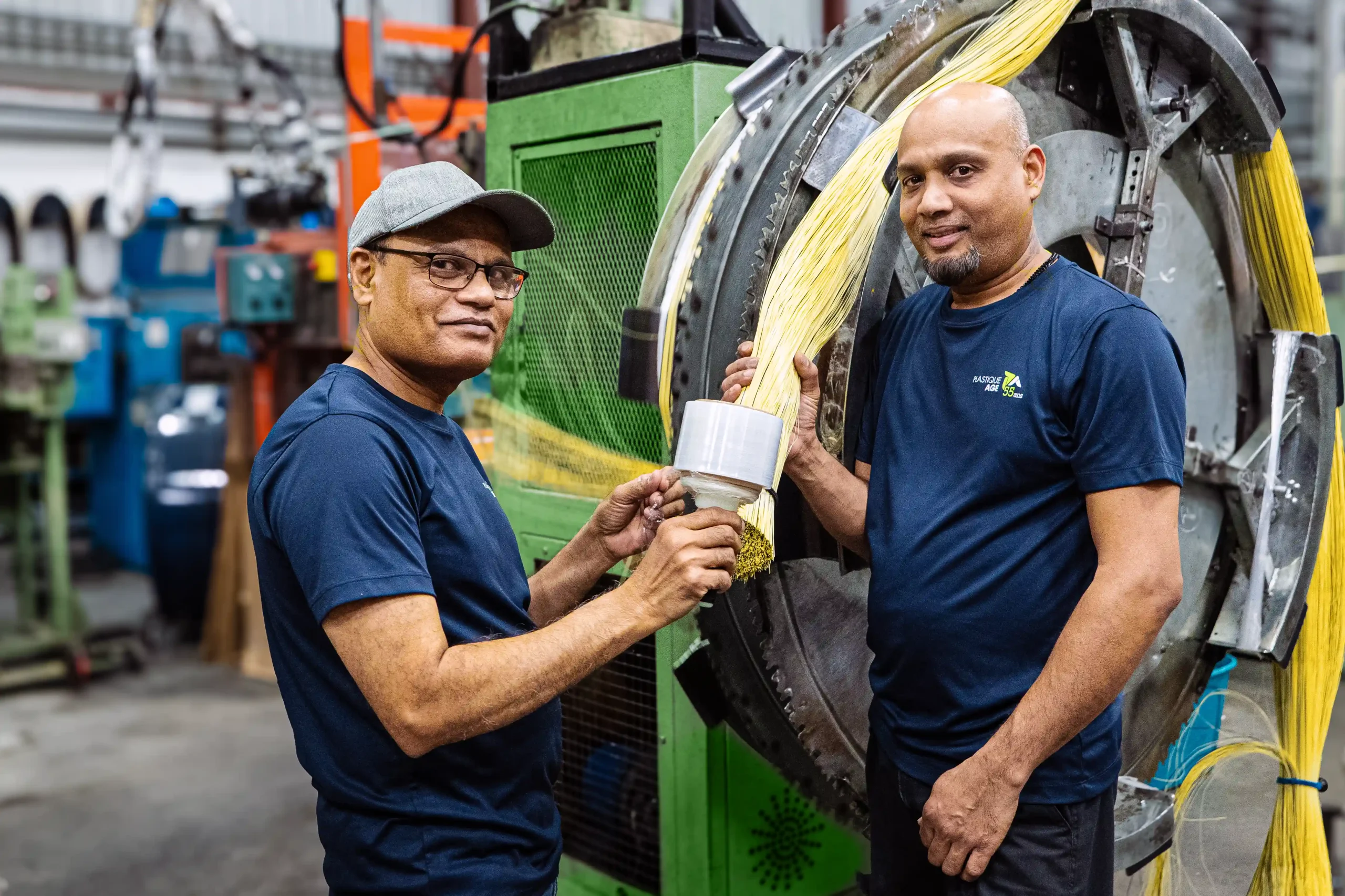 Two Plastic Age employees working on monofilament extrusion line with yellow strands